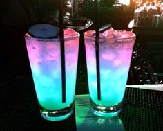 two tall glasses filled with blue and pink liquid sitting on top of a table next to each other