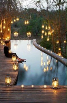 a woman sitting on the edge of a pool surrounded by lit candles and lights in front of her