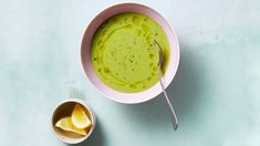 a bowl filled with green liquid next to a spoon on top of a blue surface