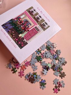 the puzzle box is filled with pieces of different colored jigsaws on a pink surface