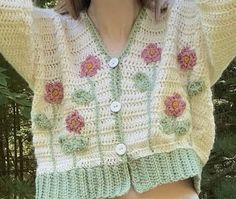 a woman wearing shorts and a crocheted cardigan in front of some trees