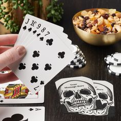 a person holding playing cards in front of a bowl of fruit and chips on a table