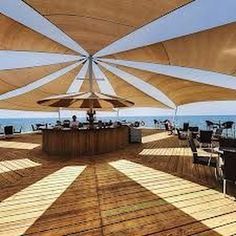 an outdoor dining area with tables and umbrellas over looking the ocean on a sunny day