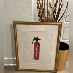 a fire extinguisher framed in a gold frame on the floor next to a potted plant