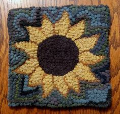 a crocheted square with a sunflower on the center is sitting on a wooden table