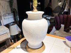 a large white vase sitting on top of a table next to a purple bowl and lamp