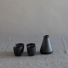 three black vases sitting next to each other on top of a table covered in linen