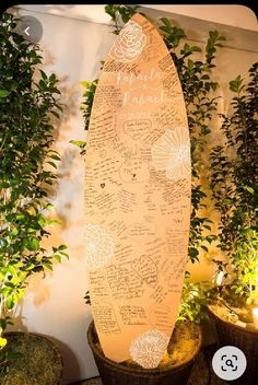 a surfboard with writing on it sitting next to potted plants