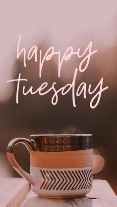 a coffee cup sitting on top of a wooden table next to a sign that says happy tuesday