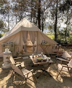 a tent is set up in the woods with chairs and tables around it for camping