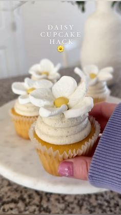 a hand holding a cupcake with white flowers on it