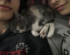 two people are cuddling with a cat on their chest and one person is wearing a hoodie