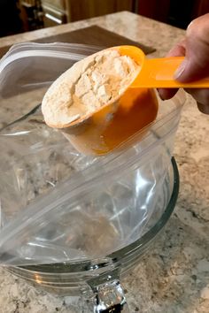 a person scooping something out of a container with an orange spoon on a marble counter top