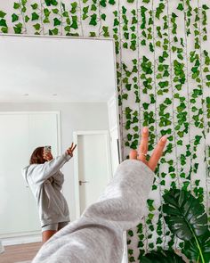 a woman taking a selfie in front of a mirror with ivy on the wall