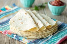 a stack of tortillas sitting on top of a blue and white towel next to small bowls filled with salsa