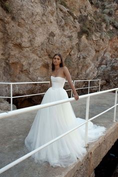 a woman in a white wedding dress standing on a bridge next to a rocky cliff