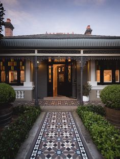 the front entrance to a house with tiled walkway and potted plants on either side