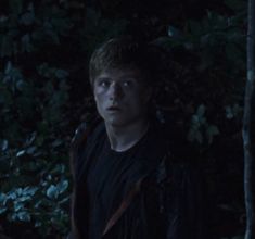 a young man standing in the woods at night with his head turned to the side