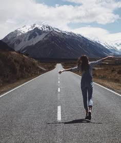 a woman walking down the middle of an empty road with her arms outstretched in the air