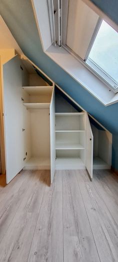 an empty room with white shelves and skylight in the roof area, next to a wooden floor