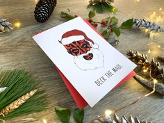 a christmas card with a santa claus face and pine cones on the table next to it