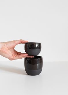 two black cups sitting next to each other on top of a white table with one hand holding the cup