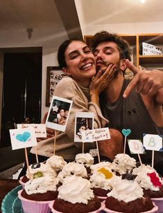 a man and woman standing next to each other in front of cupcakes with pictures on them