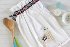 a white dress with a llama embroidered on it and two wooden spoons next to it