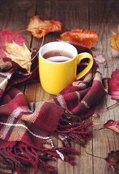 a cup of tea on a wooden table with autumn leaves around it and a plaid scarf