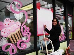 a woman is standing in front of a store window holding a paint roller and smiling at the camera