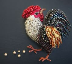 a beaded rooster brooch sitting on top of a table next to some beads