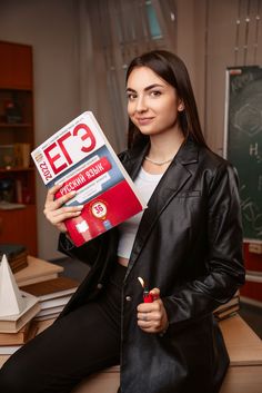 a woman sitting on a desk holding up a box of e3 and an eraser