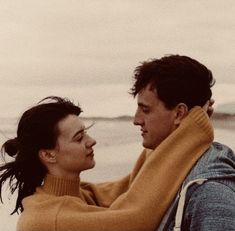 a man and woman standing next to each other on the beach looking at each other