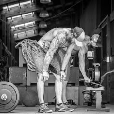 two men are doing different things in a gym together, one is holding a barbell and the other is squatting