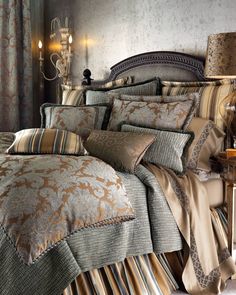 a large bed covered in lots of pillows next to a night stand with two lamps on it