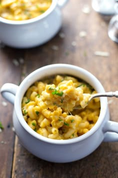 a spoon full of macaroni and cheese soup on a table with another bowl in the background