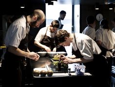 several chefs are preparing food in a restaurant kitchen while another man looks down at the table