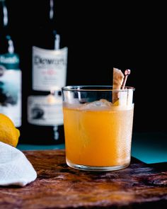 a glass filled with orange juice next to two bottles of alcohol and a lemon wedge