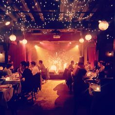 a group of people sitting at tables in a room with lights on the ceiling and red curtains