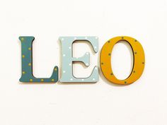 the word leo spelled with wooden letters on a white wall in front of a clock