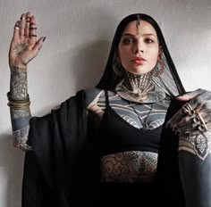 a woman with tattoos on her arms and arm sleeves, wearing a black outfit holding up two hands