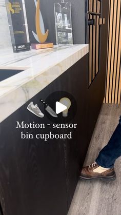 a man standing on the side of a counter next to a sign that says motion - sensor bin cupboard