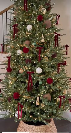 a decorated christmas tree in a basket with red ribbon and ornaments on it's top