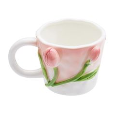 a coffee cup with pink flowers painted on the side and green stems sticking out of it