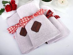 four folded towels with chocolates tied to them on a white tablecloth next to red roses