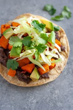 a tortilla topped with meat, vegetables and cilantro on a gray surface