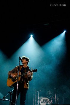 a man standing on top of a stage with a guitar in front of microphones