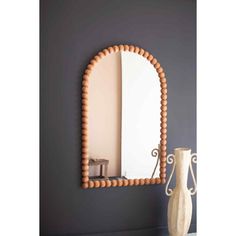 a mirror that is next to a vase on a table in front of a gray wall