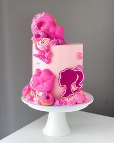 a cake with pink icing and decorations on a white pedestal in front of a gray wall