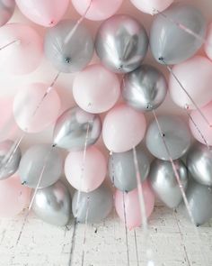 a bunch of pink and grey balloons on a white brick wall with pins sticking out of them